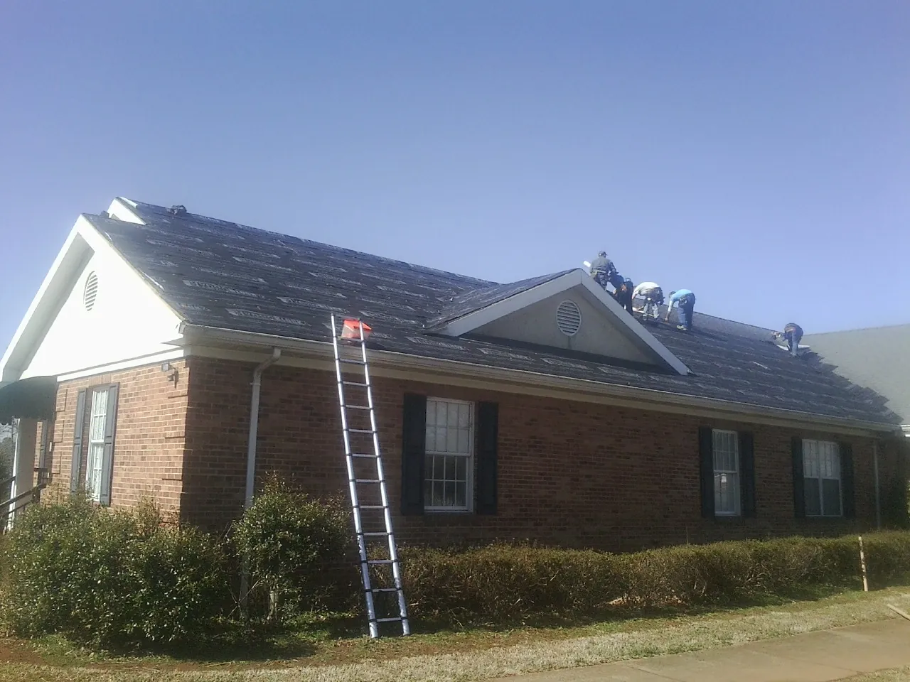 Crew tearing shingles off a brick ranch roof with a ladder set — Metal Roof Repair work by our crew in Pomfret Center
