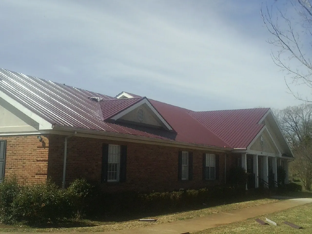 Red metal roof with gabled entries on a long brick building, from a Hail Damage Roof Repair job in Pomfret Center