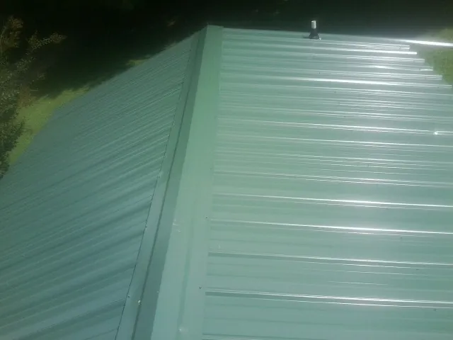 New green metal panels meeting at the ridge of a roof — Flat Roof Repair work by our crew in Pomfret Center