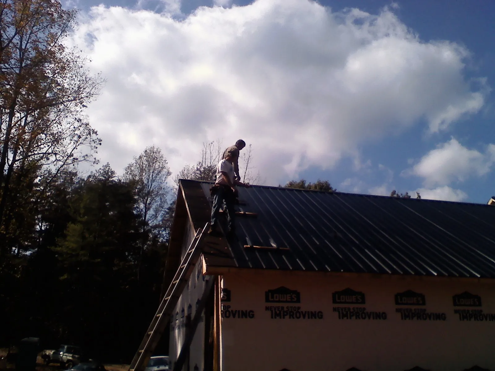 Roofer fastening dark metal panels high against a cloudy sky, from a Roof Inspection job in Pomfret Center