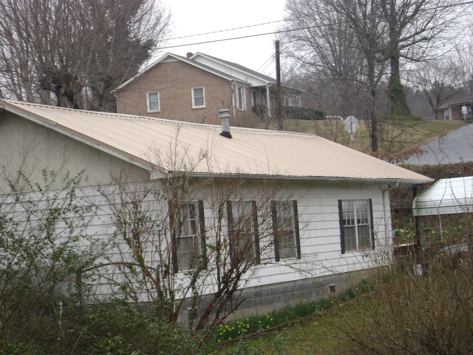 Tan metal roof on a white sided house set into a hillside — Commercial Roofing by Roofing Brothers in Pomfret Center