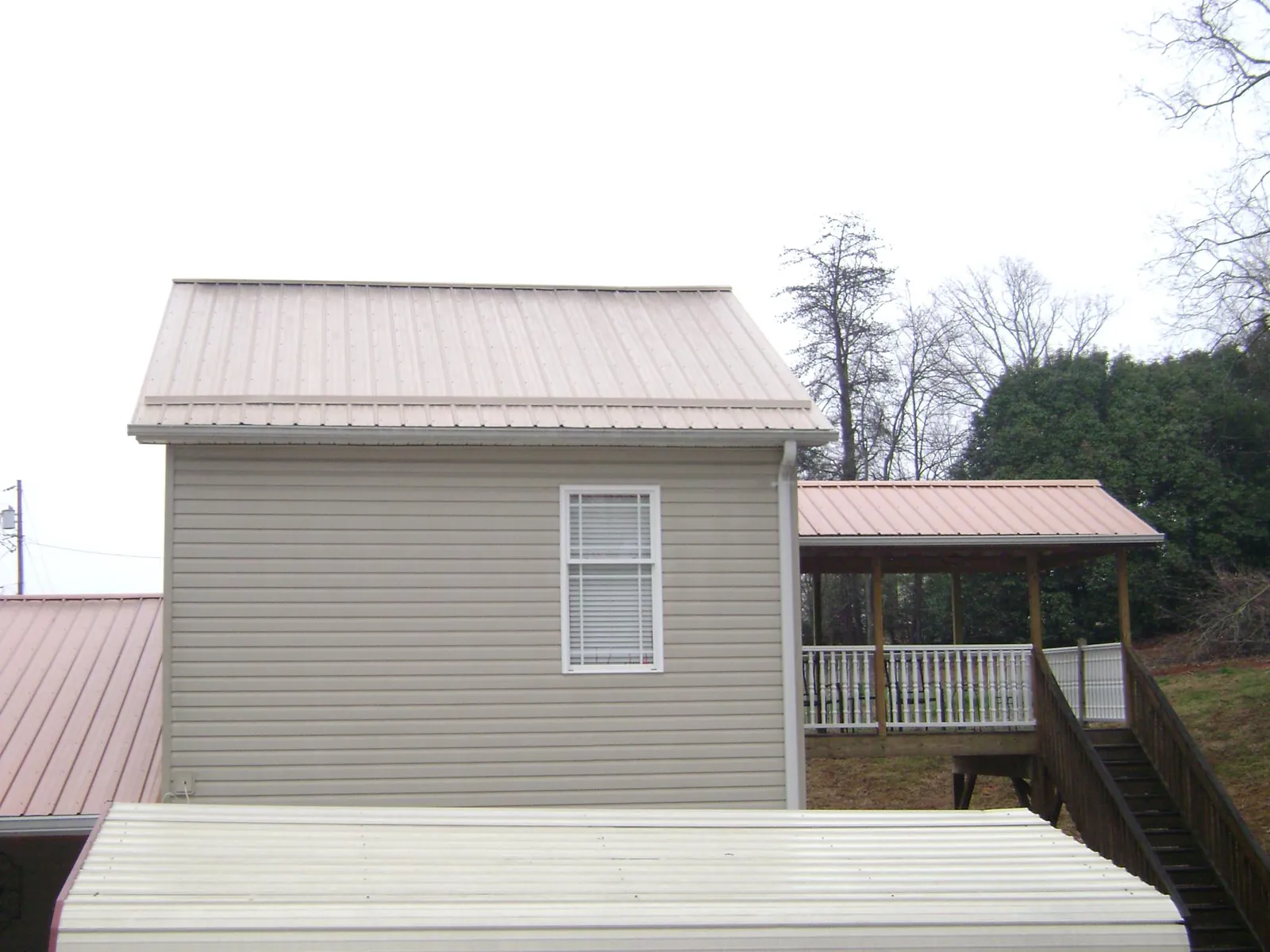 Tan metal roofs on a two story addition and attached porch, from a Roof Replacement job in Pomfret Center